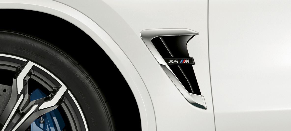 BMW X4 M, skrzela M. BMW X4 M, biel alpejska, wygląd zewnętrzny, skrzela M z chromowanymi elementami i oznaczeniem modelu.