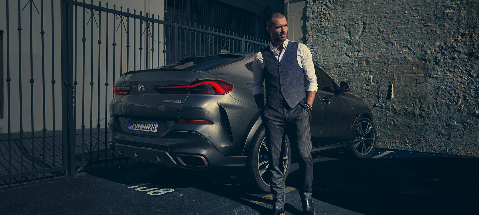 BMW X6 M50i, tylny półprofil. Mężczyzna obok BMW X6 M50i, tylny półprofil.