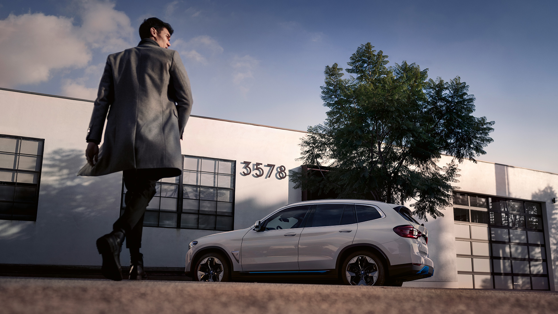 BMW iX3 G08, widok z boku przed budynkiem z mężczyzną BMW iX3 G08 2020, biel mineralna, metalizowany, widok z boku przed budynkiem z mężczyzną