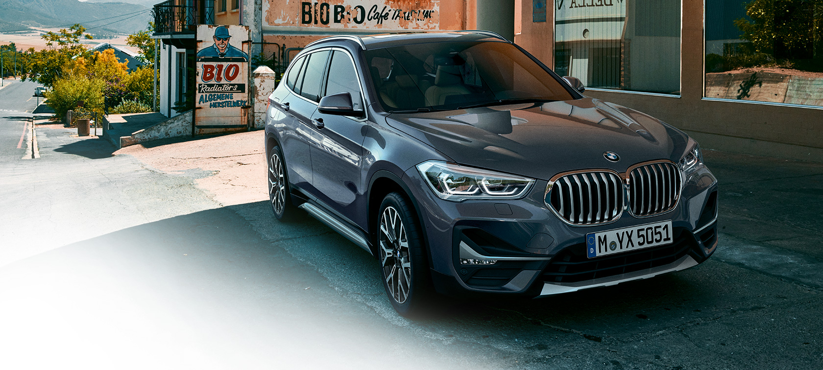 BMW X1, ujęcie z półprofilu od przodu. BMW X1, ujęcie z półprofilu od przodu, zaparkowany na tle scenerii miejskiej.