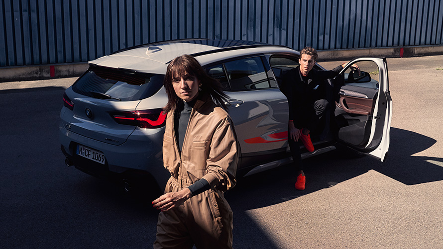 BMW X2 F39 szary Brooklyn tylny półprofil z otwartymi drzwiami i dwiema osobami BMW X2 F39 szary Brooklyn tylny półprofil z otwartymi drzwiami i dwiema osobami
