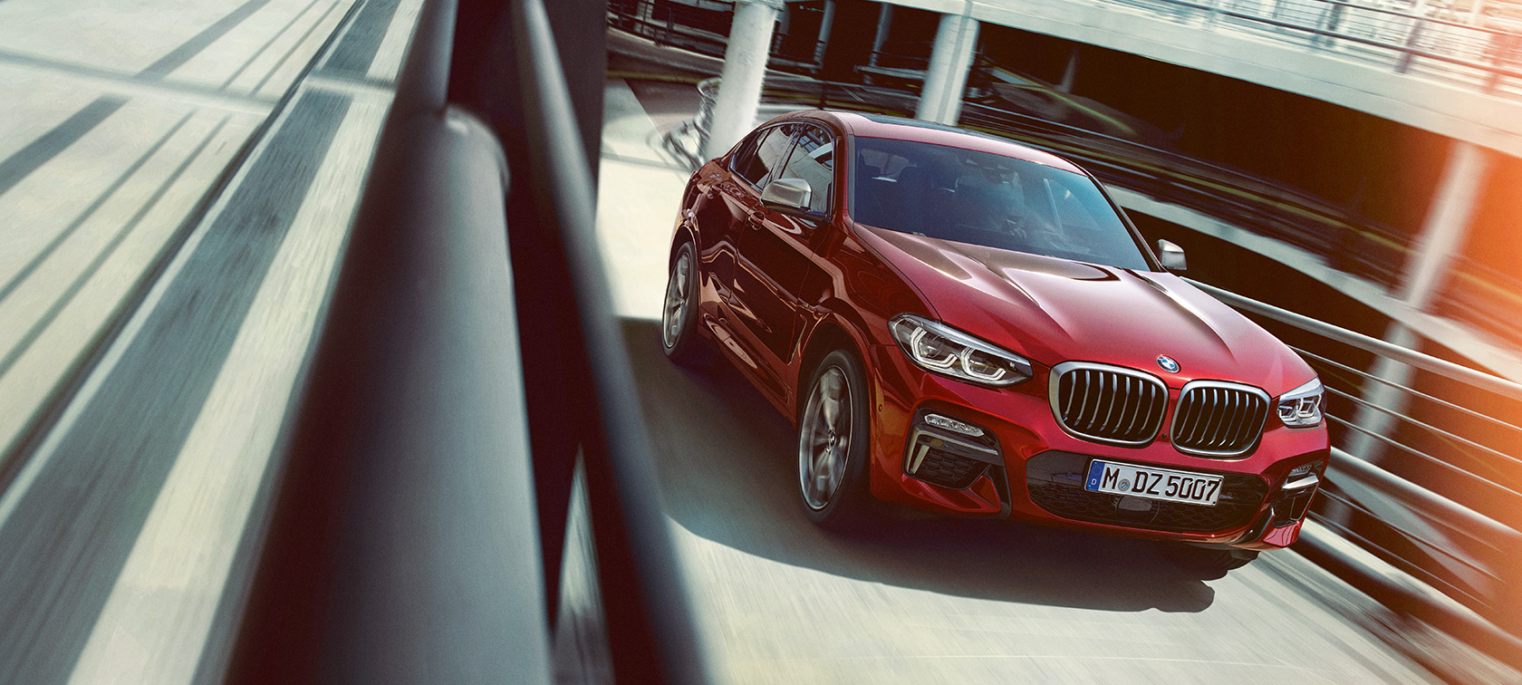 BMW X4 podczas jazdy na parkingu wielopoziomowym BMW X4 G02 2018 czerwień Flamenco z brylantowym połyskiem, półprofil z boku, podczas jazdy na parkingu wielopoziomowym