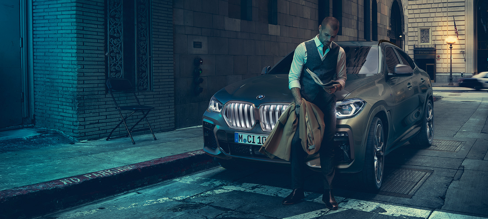 Mężczyzna opierający się o BMW X6. Mężczyzna opierający się o BMW X6 w perspektywie bocznej na tle scenerii miejskiej.