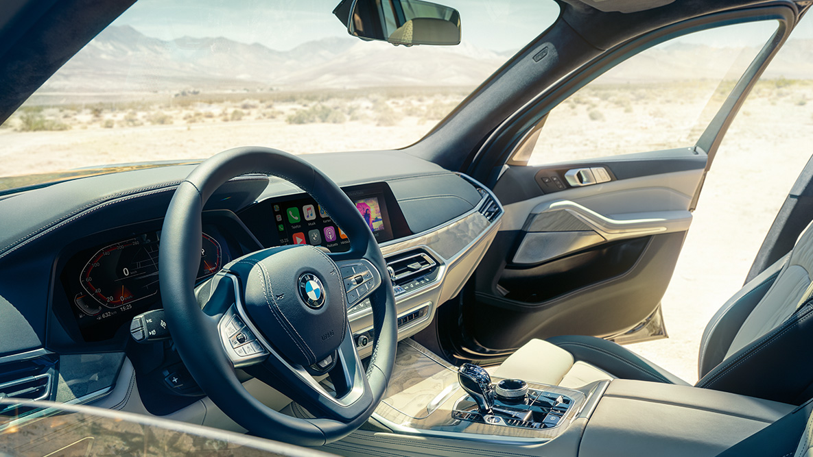 Wnętrze BMW X7: widok z zewnątrz na pierwszy rząd foteli z kierownicą, zestawem wskaźników i fotelami skórzanymi Wnętrze BMW X7