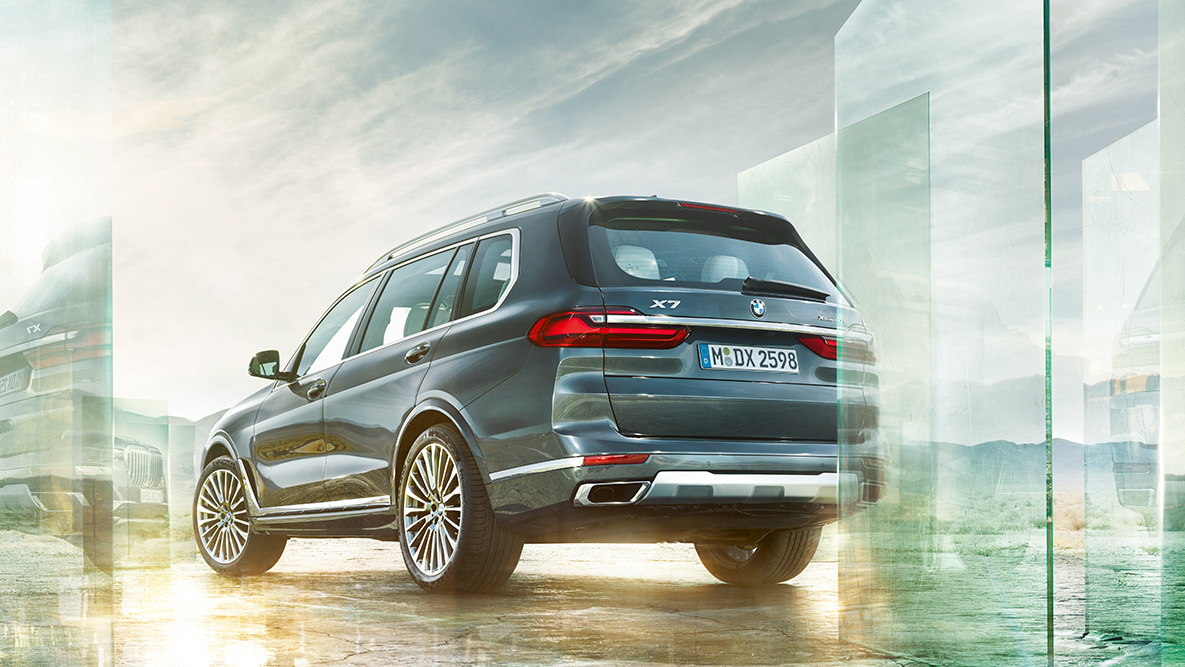 BMW X7: komfort i dynamika jazdy BMW X7 z tyłu z półprofilu na abstrakcyjnym tle