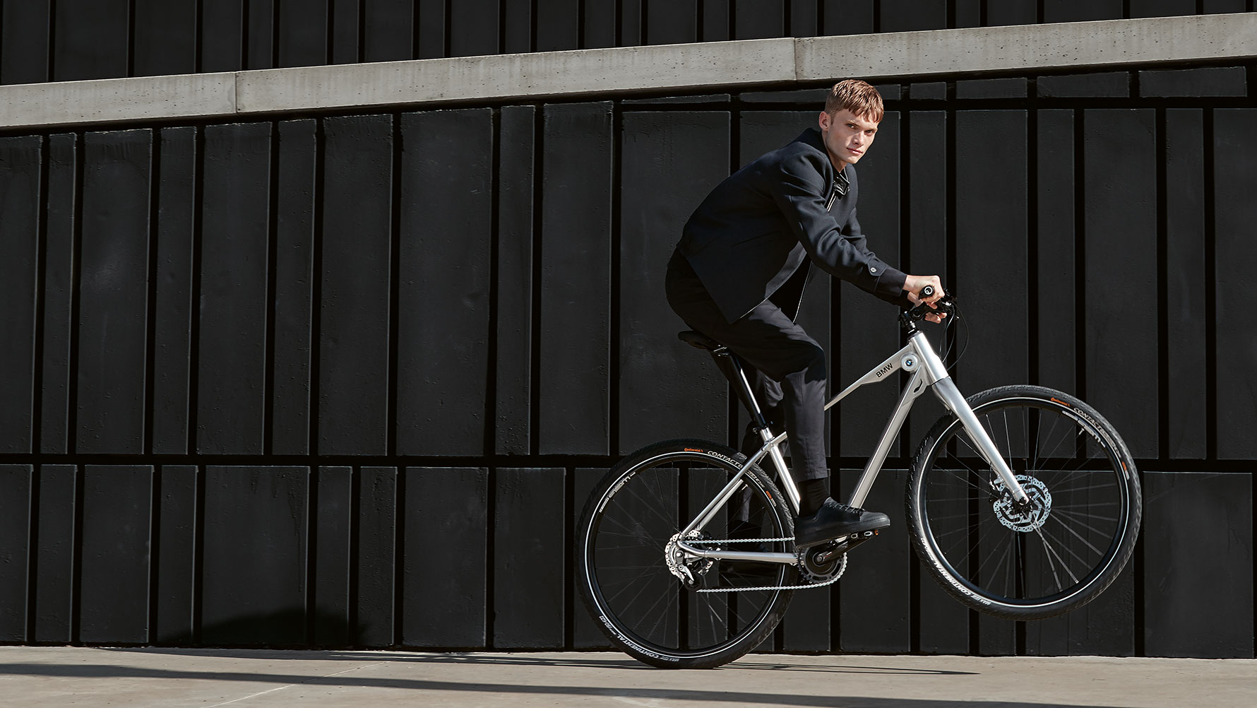 Zdjęcie przedstawia młodego mężczyznę robiącego dynamiczne wheelie na rowerze BMW Cruise Bike. Zdjęcie przedstawia młodego mężczyznę robiącego dynamiczne wheelie na rowerze BMW Cruise Bike.
