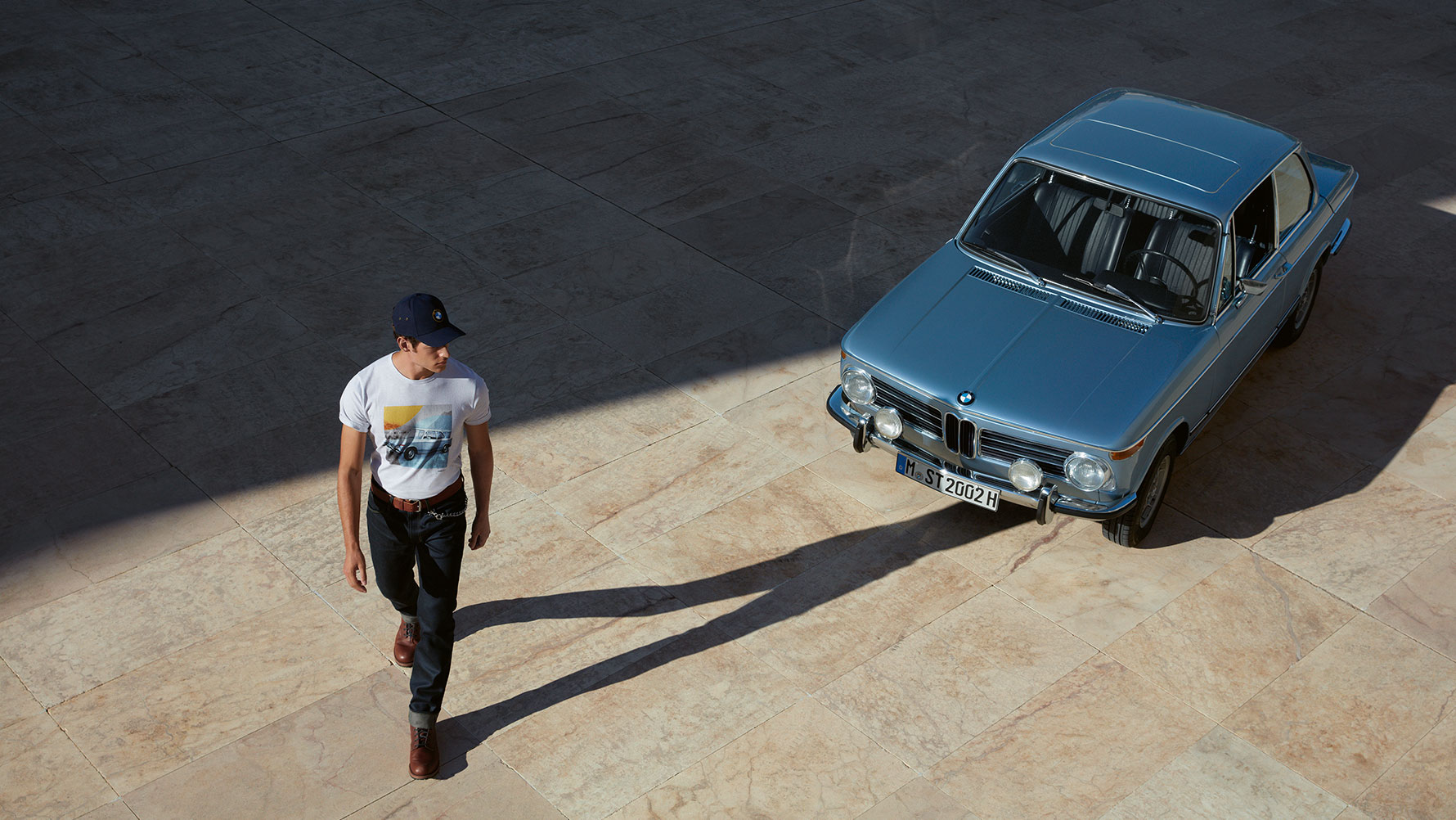Przedstawiony jest mężczyzna w męskiej koszulce BMW Classic, podziwiający klasyczny model BMW. Przedstawiony jest mężczyzna w męskiej koszulce BMW Classic, podziwiający klasyczny model BMW.