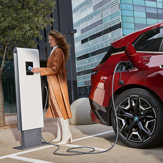 BMW iX i20 przy stacji ładowania kobieta z kartą BMW Charging