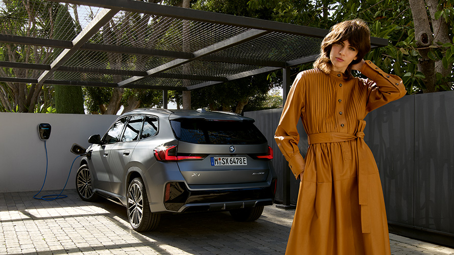 BMW X1 Hybryda Plug-In 2022 U11, widok z tyłu boku podczas ładowania z modelem BMW X1 Hybryda Plug-In 2022 U11, widok z tyłu boku podczas ładowania z modelem