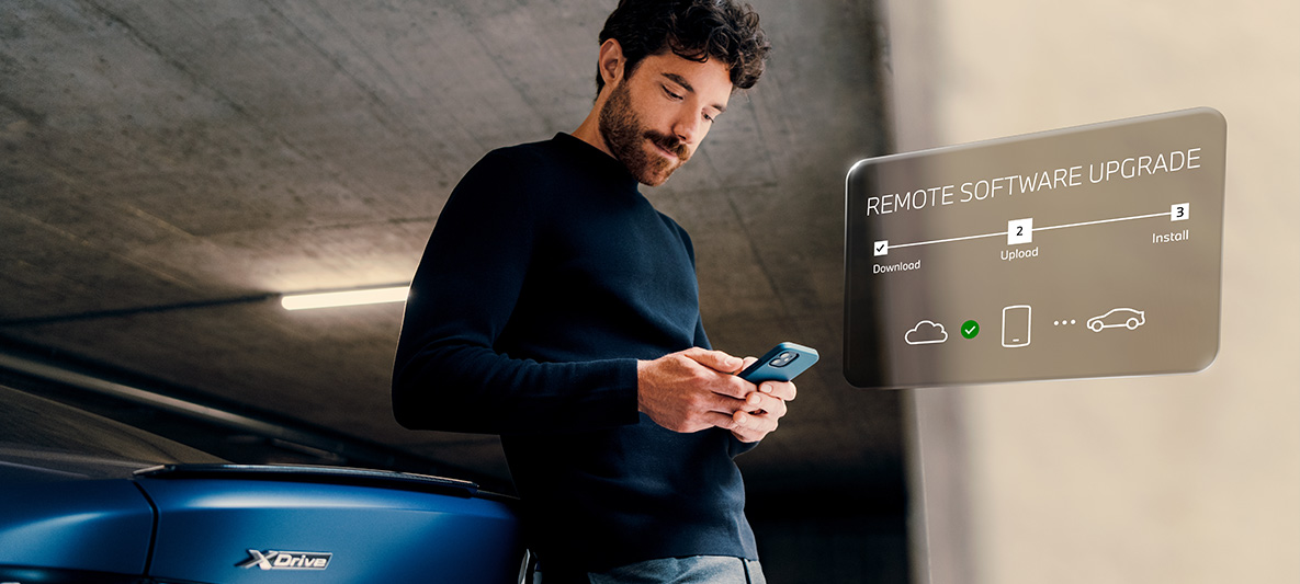 Mężczyzna opiera się o tył BMW i patrzy na swój smartfon Zdalna aktualizacja oprogramowania mężczyzna opiera się o tył BMW i patrzy na swój smartfon