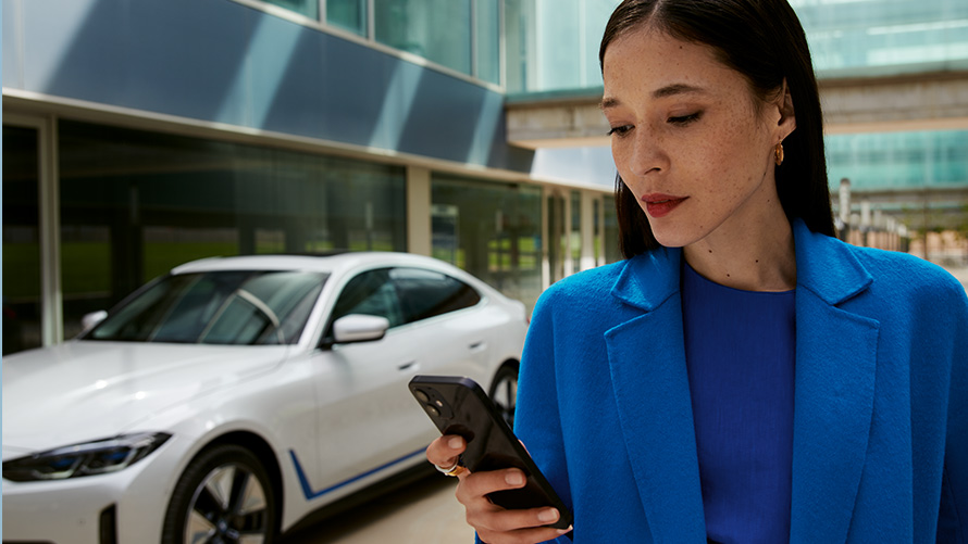 Kobieta stoi przed BMW Kobieta stoi przed BMW i patrzy na swojego smartfona