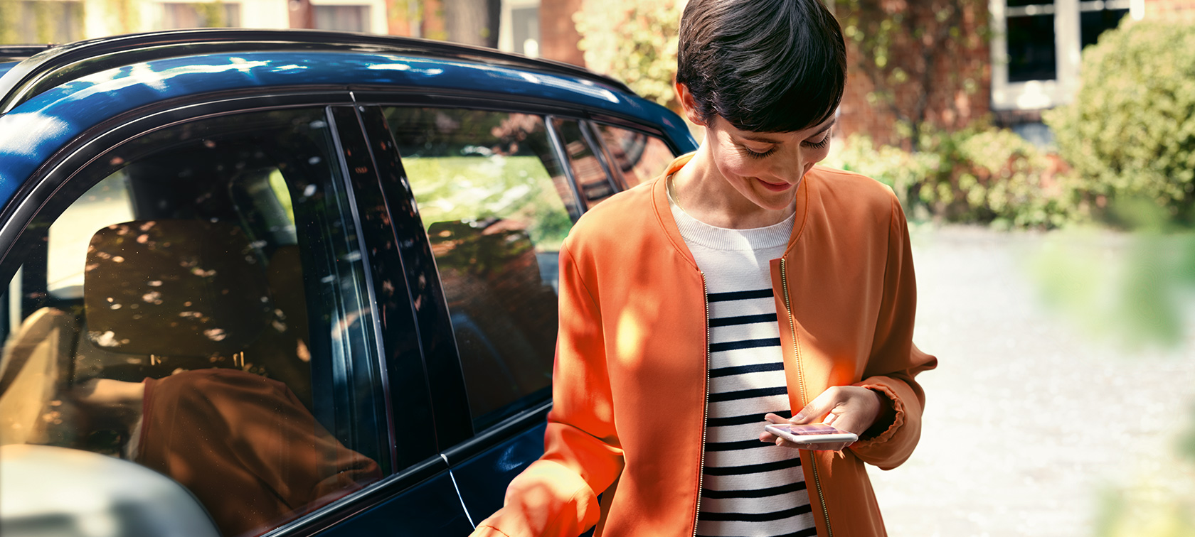 Brunetka przed BMW Brunetka w pomarańczowej kurtce przed BMW patrzy na swój smartfon