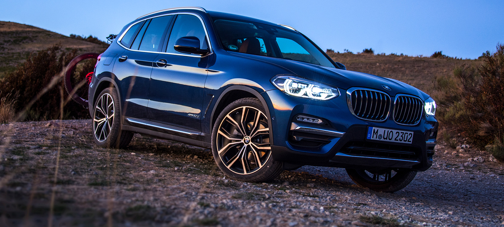 Granatowe BMW X3 w terenie Zaparkowane granatowe BMW X3 z bagażnikiem tylnym i rowerem górskim w terenie