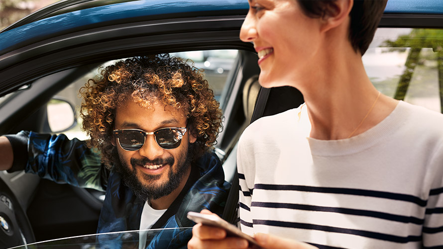 BMW Connected Mężczyzna w BMW i kobieta obok BMW używający BMW Connected na swoich smartphonach