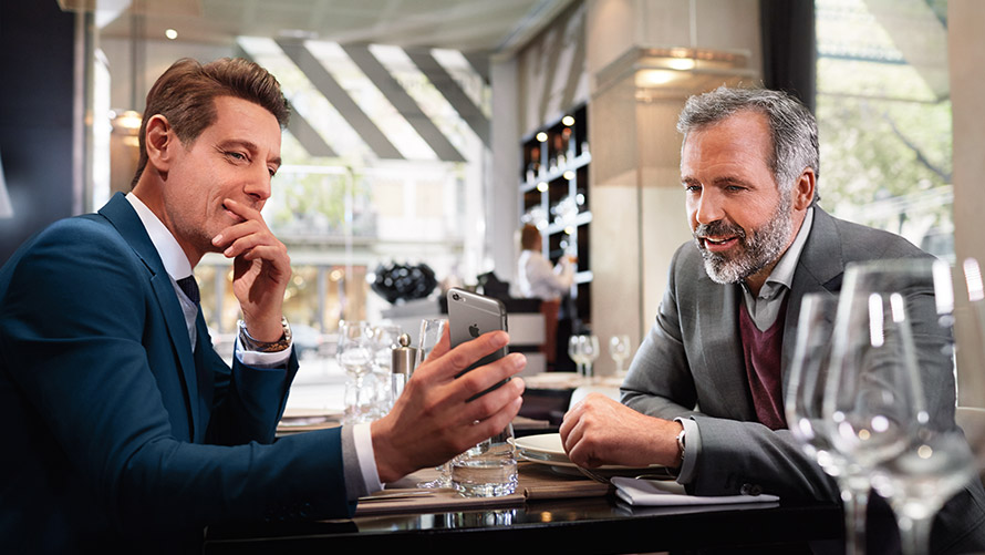 "Zarządzaj swoimi ulubionymi lokalizacjami" Dwóch mężczyzn w restauracji używają funkcji "Zarządzaj swoimi ulubionymi lokalizacjami" na smartfonie