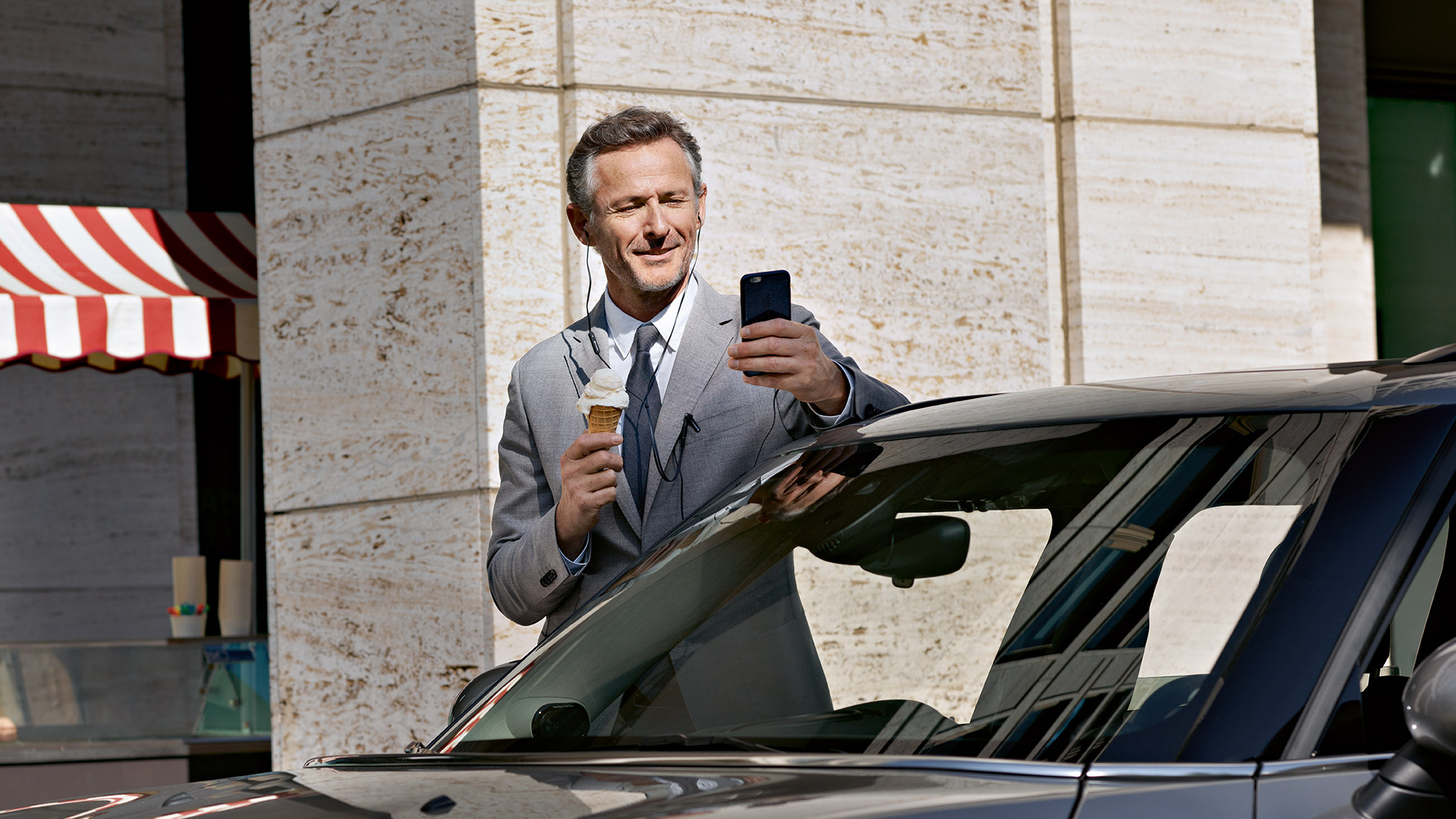 BMW Corporate Aftersales, kontrola kosztów BMW Corporate Aftersales: mężczyzna je lody i sprawdza finanse na smartfonie