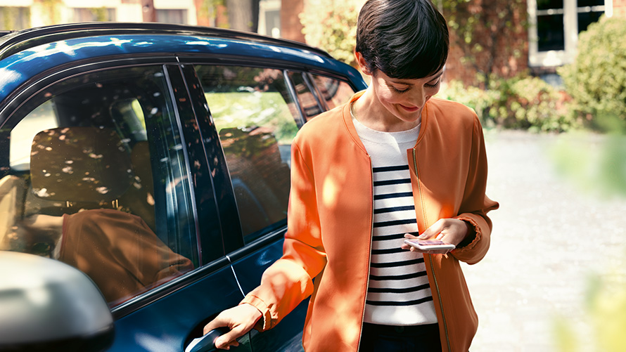 BMW TeleService Kobieta ze smartfonem stoi przy drzwiach swojego BMW