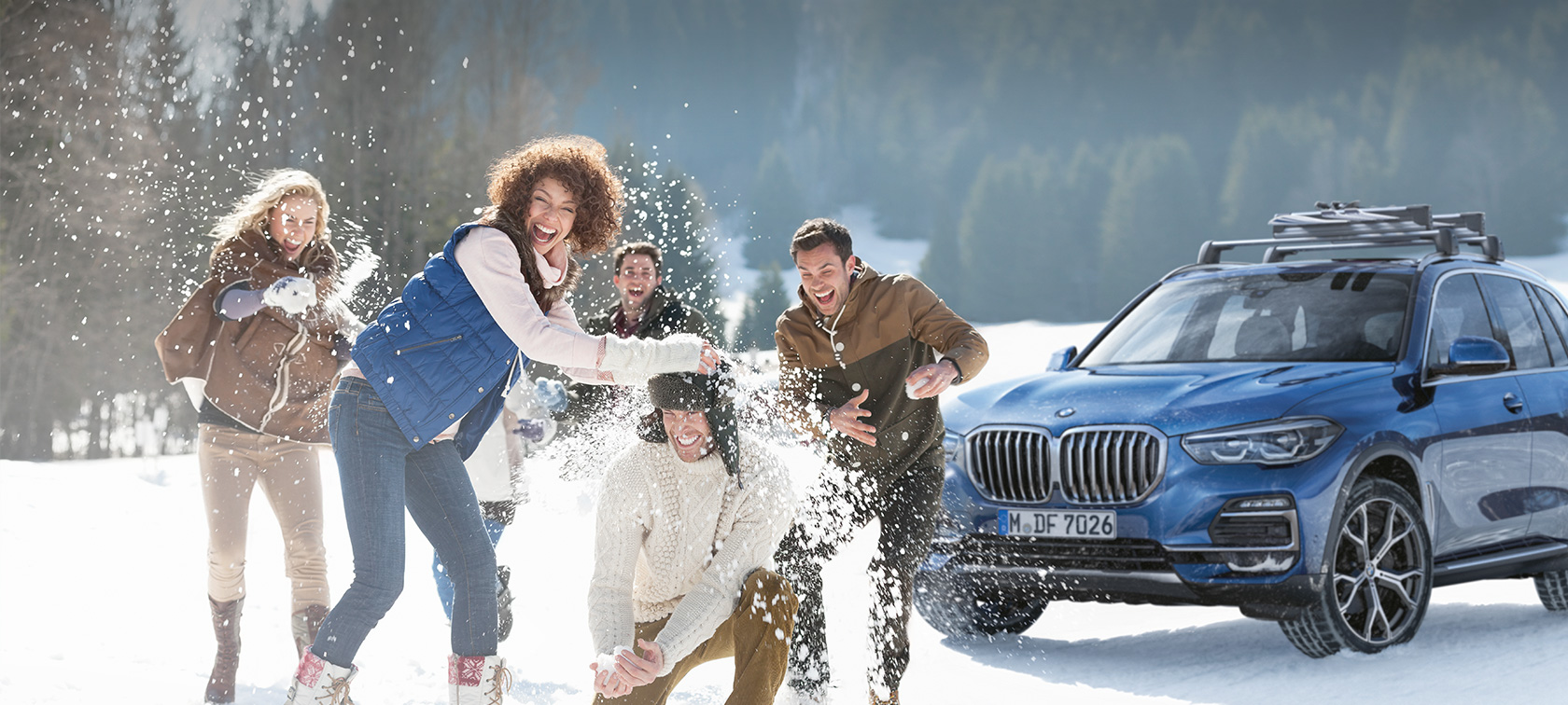 Oryginalne akcesoria BMW i Serwis BMW na jesień i zimę Kobiety i mężczyźni śmieją się na śniegu przed BMW