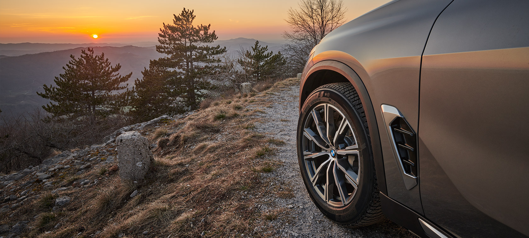 Oryginalne obręcze kół BMW w BMW X5 (G05 LCI) na drodze szutrowej na zboczu góry o zachodzie słońca Oryginalne obręcze kół BMW w BMW X5 (G05 LCI)