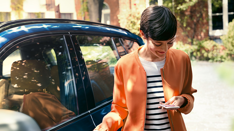 Oferta letnia BMW BMW Teleservices Oferta letnia BMW BMW Teleservices kobieta stoi przed BMW I używa smartfona