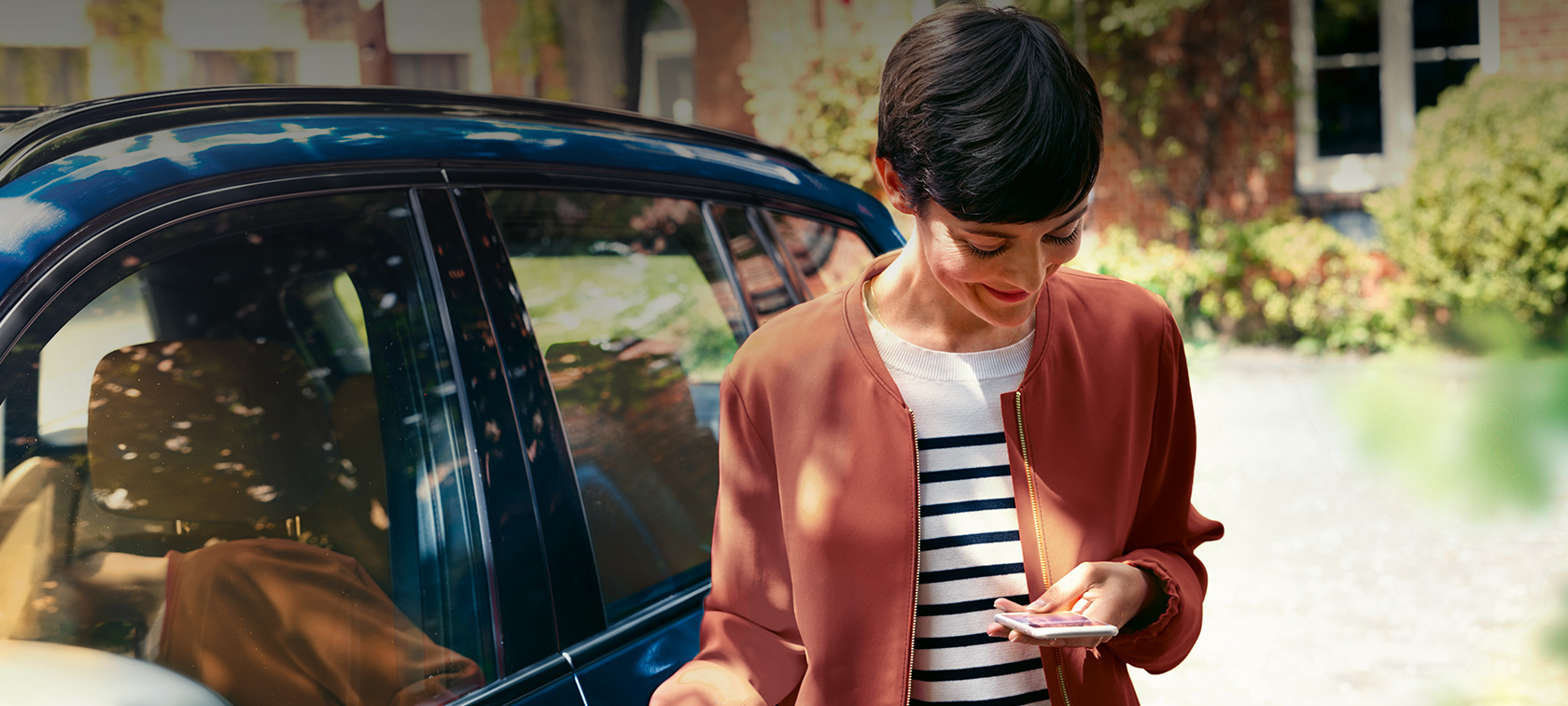 BMW TeleService kobieta patrząca na smartfona BMW TeleService kobieta przed BMW patrząca na smartfona