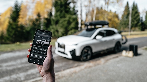 Telefon z uruchomioną aplikacja My BMW App i BMW iX z akcesoriami w tle. Telefon z uruchomioną aplikacja My BMW App i BMW iX z akcesoriami w tle.