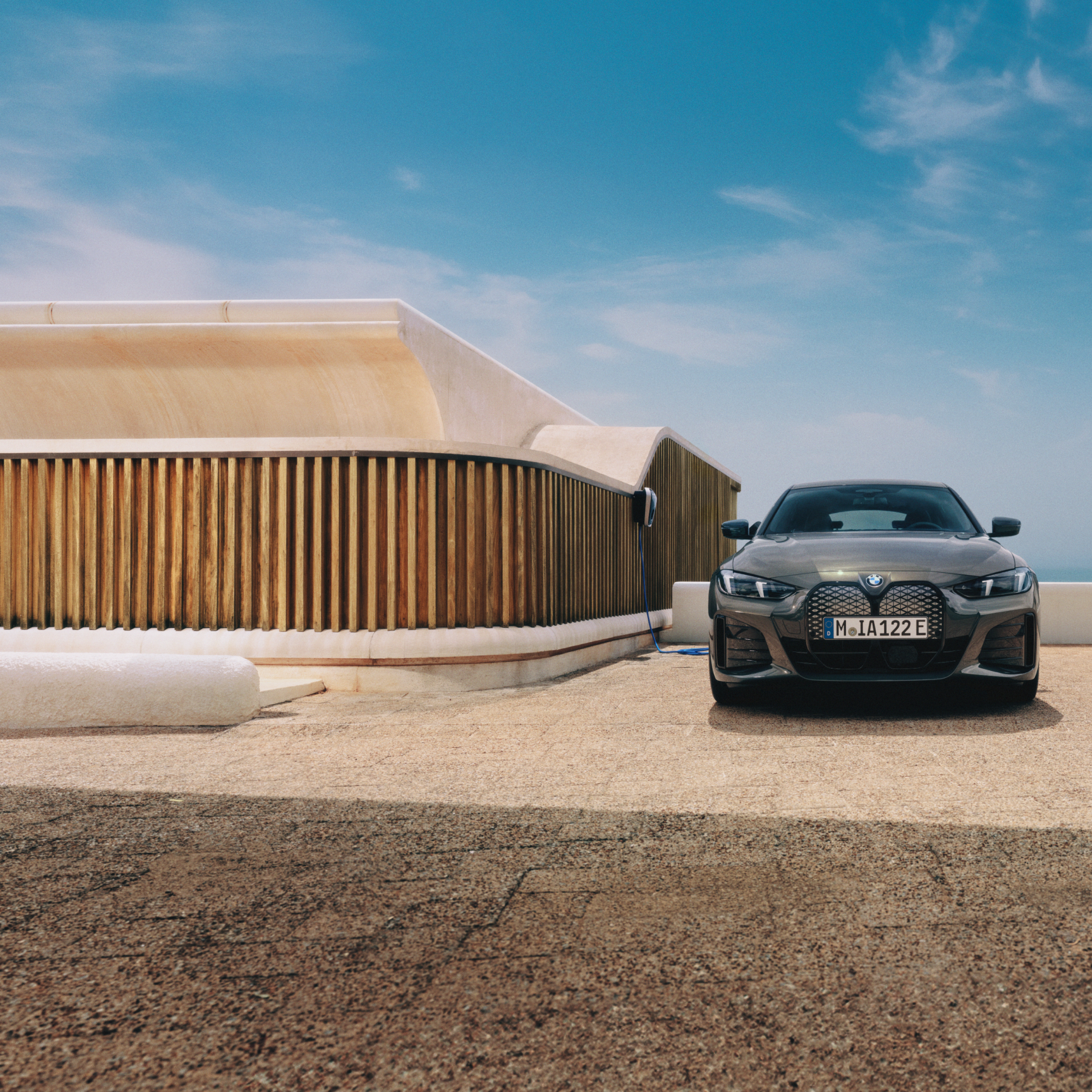 Mężczyzna ze smartfonem stoi obok BMW i4 podłączonego do stacji Wallbox