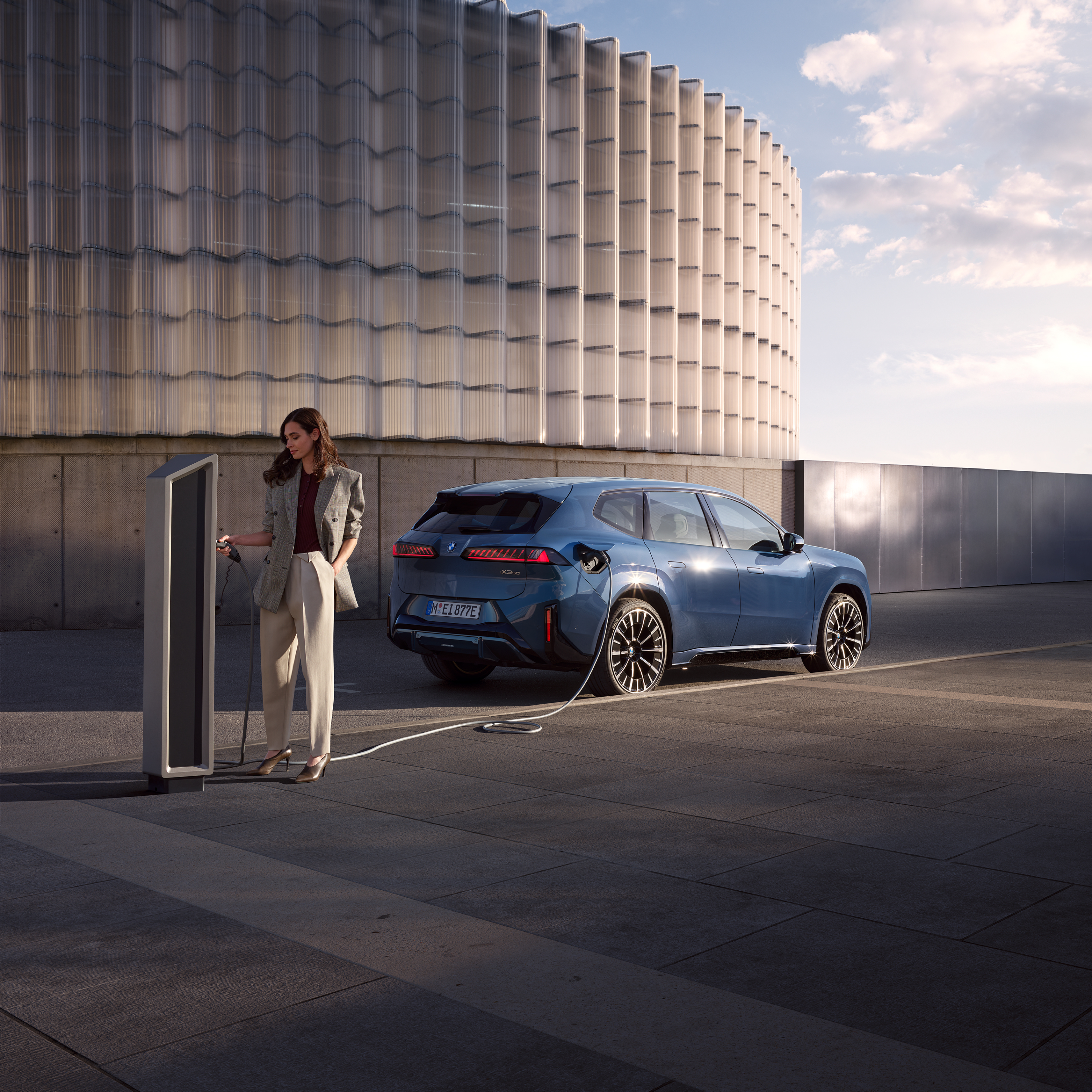 Kobieta stoi obok BMW iX 3, które jest podłączone do publicznego terminala ładującego